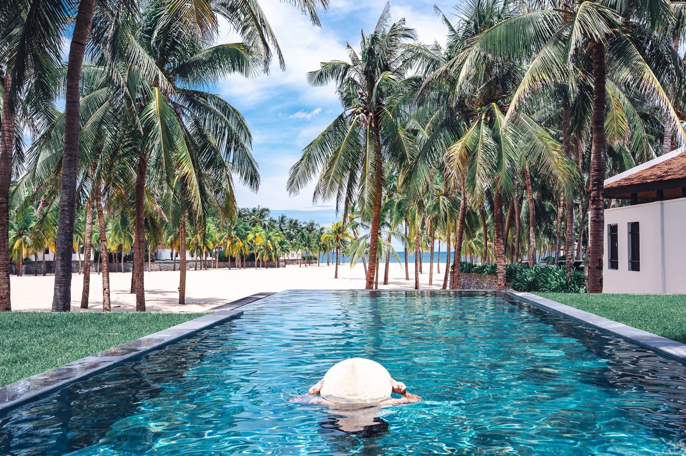 The private pool at the Four Seasons Nam Hai A woman wearing a Vietnamese conical hat while paddling in The private pool at the Four Seasons Nam Hai